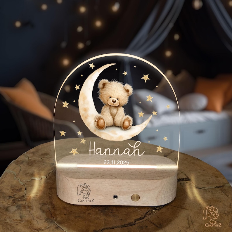 A wooden nightstand with a clear glass front, featuring a teddy bear sitting on a crescent moon and surrounded by stars. The bear is wearing a crown and the name "Hannah" is written below it.