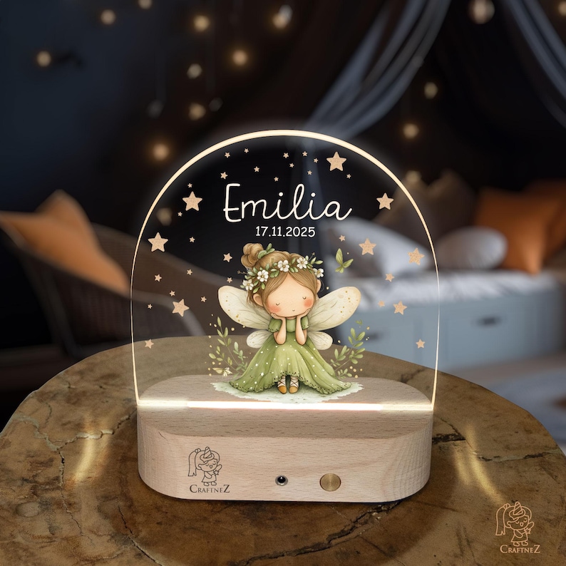 A wooden nightstand with a glass display case on top, featuring a fairy-like character with wings and a flower crown. The fairy is surrounded by stars and the name "Emilia" is written above her.