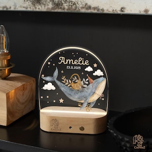 A lighted glass display with a whale and stars, displaying the name "Amelie" and the date "23.11.2025".