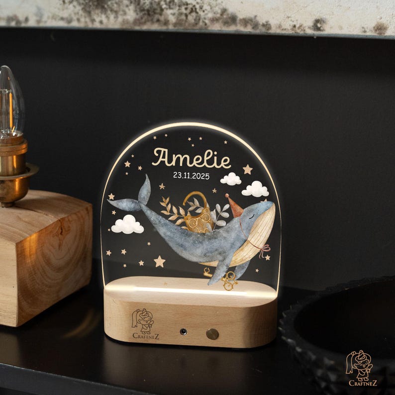 A lighted glass display with a whale and stars, displaying the name "Amelie" and the date "23.11.2025".