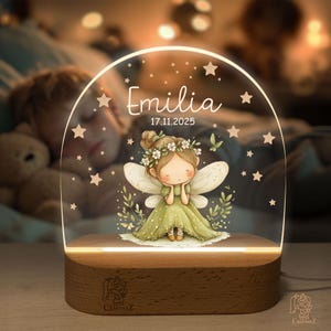 A glass-topped nightstand with a fairy figurine and a nameplate displaying the name 'Emilia'.