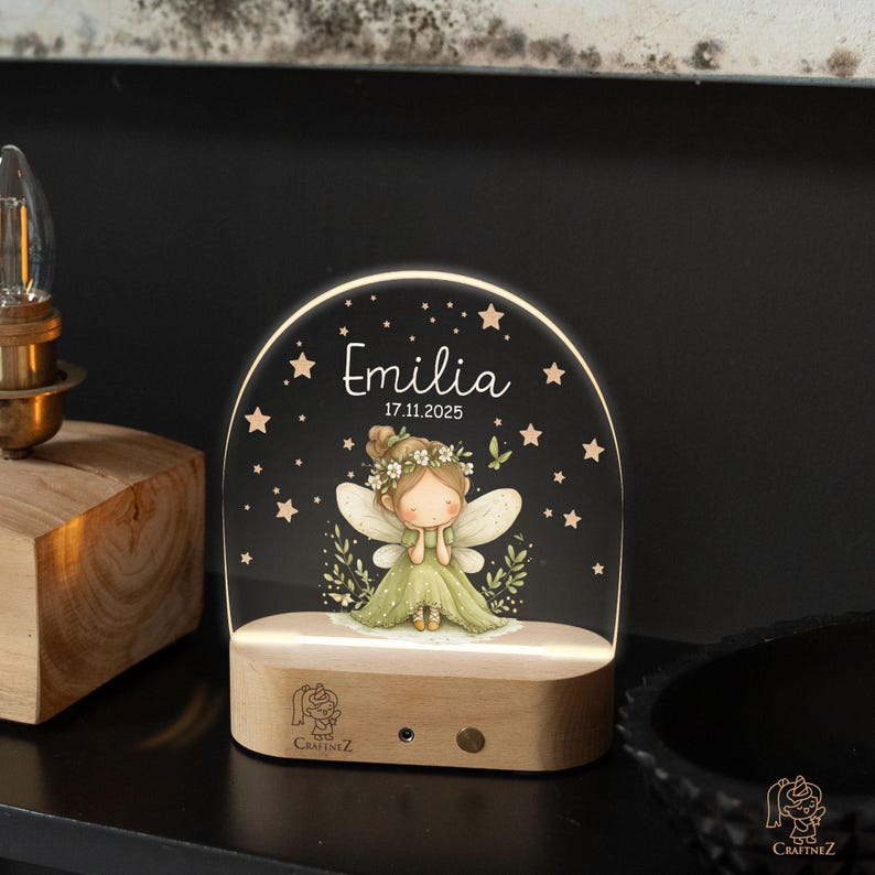 A lighted display featuring a fairy with wings and a flower crown, surrounded by stars, with the name 'Emilia' and the date '17.11.2025' displayed on it.
