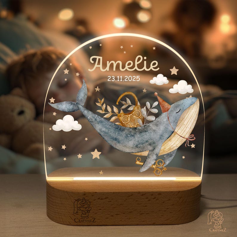 A personalized glass light stand with a whale and stars, displaying the name "Amelie" and the date "23.11.2025".