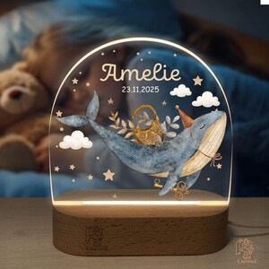 A personalized lighted display featuring a whale and a teddy bear, with the name "Amelie" and the date "23.11.2025" displayed on it.