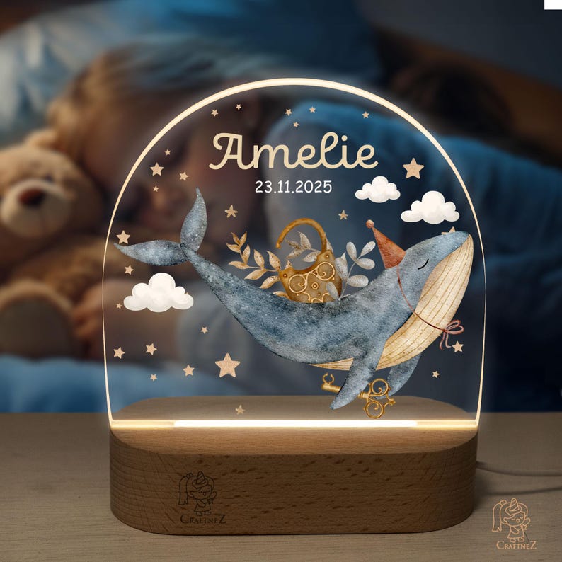 A personalized lighted display featuring a whale and a teddy bear, with the name "Amelie" and the date "23.11.2025" displayed on it.