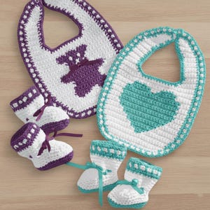 May include: A set of crocheted baby bibs and booties. The bibs are white with purple and teal detailing, with a teddy bear and heart design. The booties are white with matching accents and ribbon ties. A handmade baby gift.