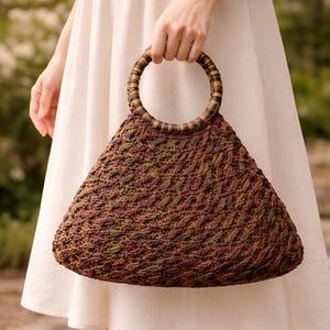 May include: A brown, triangular-shaped handbag with a woven texture and a circular handle. The bag features a mix of brown and green threads, creating a textured pattern. The handle is made of a similar material, with alternating brown and tan stripes.
