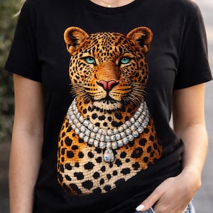 May include: Black t-shirt featuring a detailed illustration of a leopard's face with blue eyes and a diamond necklace. The leopard has a spotted coat and is centered on the shirt. The shirt has short sleeves.
