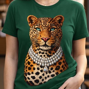 May include: Green t-shirt featuring a detailed leopard illustration with a diamond necklace. The leopard has a spotted coat, blue eyes, and a pink nose. The shirt is a solid dark green color.
