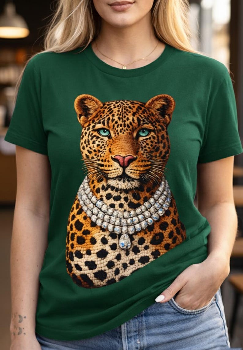 May include: Green t-shirt featuring a detailed leopard illustration with a diamond necklace. The leopard has a spotted coat, blue eyes, and a pink nose. The shirt is a solid dark green color.