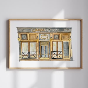 Könnte beinhalten: Aquarellmalerei eines Pariser Ladens mit der Aufschrift "Chapi Chapo" über dem Eingang. Das Gebäude hat eine dunkelgraue Fassade, Holzfensterrahmen und einen kleinen Balkon. Das Kunstwerk ist in einem hellbraunen Holzrahmen gerahmt.