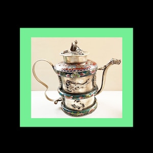 May include: A silver teapot with a dragon design and colorful enamel accents. The teapot has a lid with a finial and a spout shaped like a dragon's head.