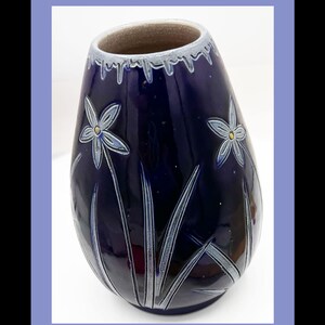 May include: A dark blue ceramic vase with a glossy finish. The vase features a floral design with white and light blue accents. The vase has a unique shape and a textured rim, suitable for home decor.