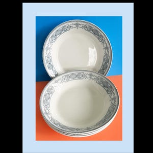 May include: A stack of white ceramic bowls with a blue and white decorative border. The bowls are set against a blue and orange background. The bowls have a simple, elegant design.