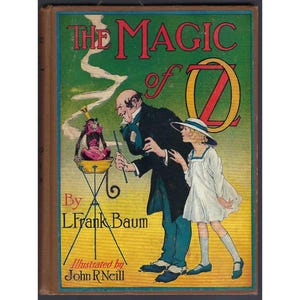 May include: A hardcover book titled The Magic of Oz by L. Frank Baum, illustrated by John R. Neill. The cover features a green and yellow background with a man in a black coat and a person in a white dress observing a monkey in a yellow bowl.