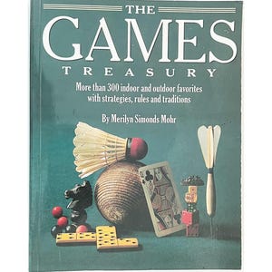 May include: A hardcover book titled The Games Treasury by Merilyn Simonds Mohr. The dark green cover features a white badminton shuttlecock, a brown wooden ball, a black chess knight, red marbles, yellow dominoes, a queen playing card, and a dart.