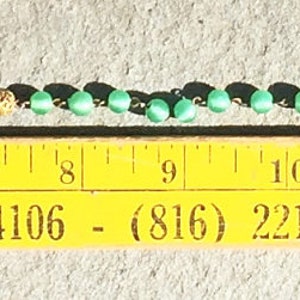 K&ouml;nnte beinhalten: Eine Nahaufnahme eines Lineals, das eine Reihe schwarzer und gr&uuml;ner Perlen misst. Das Lineal ist gelb mit schwarzen Markierungen und dem aufgedruckten Text "114 Holmes St., Kansas City, Mc. 64106 - (816) 221-6466 - BEACON AUTO".