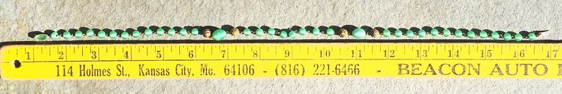 K&ouml;nnte beinhalten: Eine Nahaufnahme eines Lineals, das eine Reihe schwarzer und gr&uuml;ner Perlen misst. Das Lineal ist gelb mit schwarzen Markierungen und dem aufgedruckten Text "114 Holmes St., Kansas City, Mc. 64106 - (816) 221-6466 - BEACON AUTO".