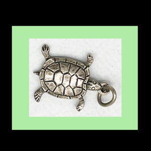 May include: Silver turtle charm with a detailed shell and a ring for attaching to a necklace or bracelet.