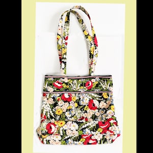 May include: A floral tote bag with a black background and a colorful pattern of red, yellow, and white flowers. The bag has two handles and a quilted design. The bag is rectangular and has a black trim.
