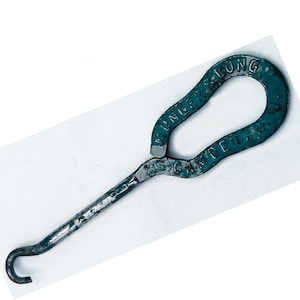 May include: A dark teal metal tool with a long handle ending in a hook and a large loop at the top. The metal surface shows signs of wear and texture. Embossed text on the loop reads MUNGER'S LONG CAMDEN NJ, with additional text near the handle base.