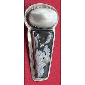 May include: A silver pendant featuring a smooth, oval-shaped white stone at the top and a long, trapezoidal black stone below. The black stone contains intricate, branching white inclusions that resemble coral or dendritic patterns set in a polished metal frame.
