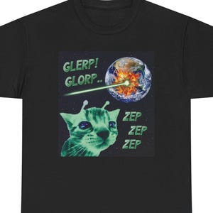 以下が含まれることがあります： 黒いTシャツ。緑色の宇宙猫のグラフィックと「GLERP！GLORP..」と「ZEP ZEP ZEP」の文字。地球がレーザービームで攻撃されている様子が描かれています。猫は触角があり、心配そうな表情をしています。