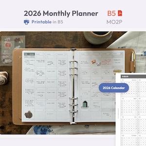 Può includere: Un'agenda mensile 2026 in un raccoglitore color cuoio con meccanismo ad anelli in metallo. Le pagine aperte presentano una griglia con note scritte a mano e piccoli adesivi. Un foglio separato mostra un calendario completo per il 2026.