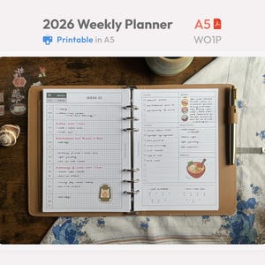 May include: A 2026 weekly planner in an A5 size binder with a tan cover. The open pages feature a grid layout for weekly scheduling, a to-do list, and a section for highlights. The planner includes a metal ring mechanism and a pen holder.