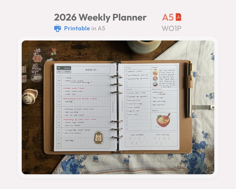 May include: A 2026 weekly planner in an A5 size binder with a tan cover. The open pages feature a grid layout for weekly scheduling, a to-do list, and a section for highlights. The planner includes a metal ring mechanism and a pen holder.