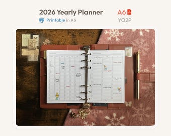 Può includere: Un'agenda annuale 2026 formato A6 aperta con una copertina in similpelle marrone e un meccanismo a rulli in metallo. Le pagine bianche presentano un layout verticale con note scritte a mano e piccoli adesivi colorati.