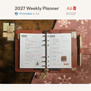 Op de afbeelding: Een bruine A6 leren ringbandplanner open op een weekoverzicht met ruitjespapier. De pagina's bevatten de tekst 2027 Weekly Planner, A6 en WO2P. De planner bevat handgeschreven notities, kleine decoratieve stickers en een gouden pen in een lus.