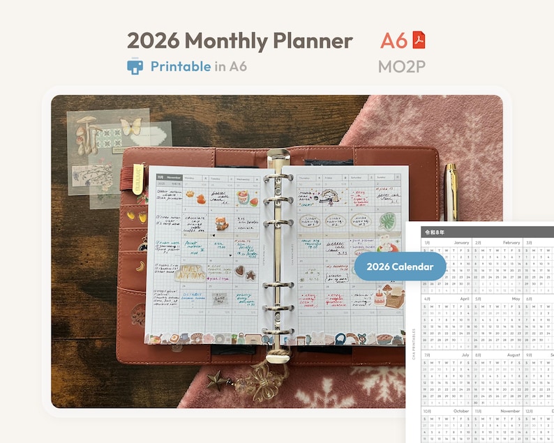K&ouml;nnte beinhalten: Ein monatlicher Planer f&uuml;r 2026 im A6-Format mit einem braunen Einband in Lederoptik und einem Metallmechanismus mit sechs Ringen. Die offenen Seiten zeigen einen Rasterkalender mit handschriftlichen Notizen und Aufklebern.