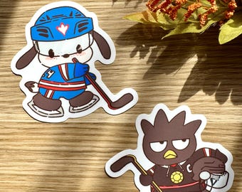 May include: Two die-cut stickers featuring cartoon characters playing hockey. One is a white dog wearing a blue helmet and jersey, holding a hockey stick. The other is a black bird wearing a hockey uniform and holding a hockey stick.
