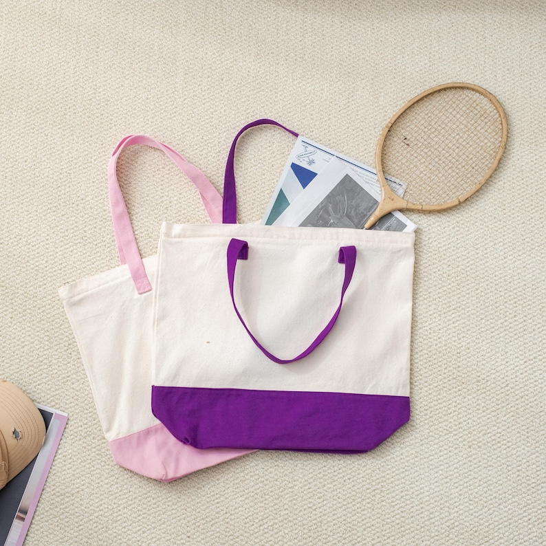 a white tote bag with purple trim, a tennis racket, and a magazine or newspaper on a beige carpeted floor.