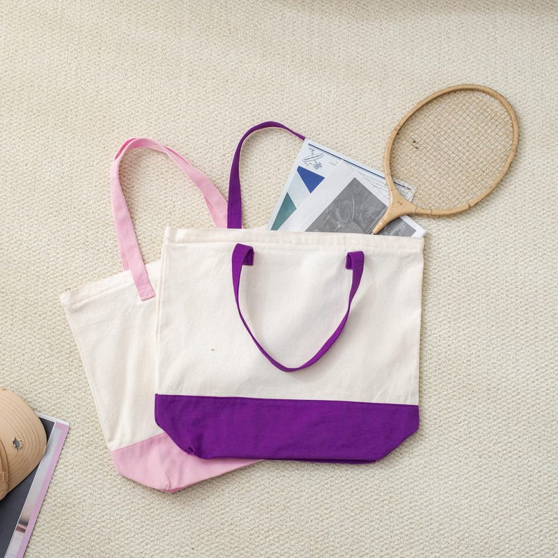 a white tote bag with purple trim, a tennis racket, and a magazine or newspaper on a beige carpeted floor.