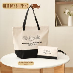 May include: A canvas tote bag and matching pouch set. The tote bag is cream-colored with a black bottom and handles. The pouch is cream-colored with a black bottom. Both feature a seashell, turtle, and starfish design with the text "Be still and know that I am God, Psalm 46:10."