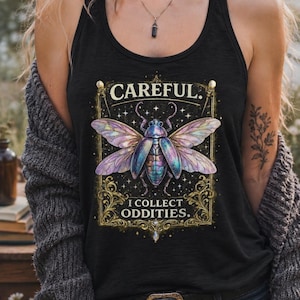 May include: A black tank top featuring a graphic print of an iridescent beetle with large wings. The design is framed by gold ornate borders and includes the text "CAREFUL. I COLLECT ODDITIES." set against a dark background with small white stars.