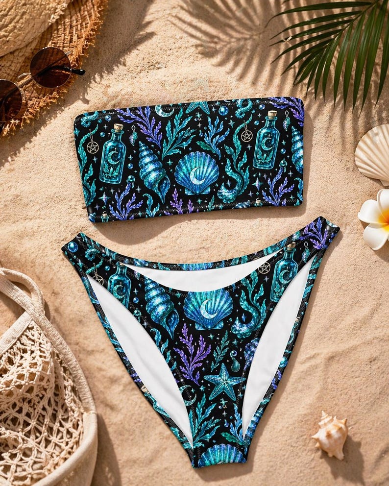 May include: A black two-piece bikini set featuring a repeating pattern of teal and purple seashells, potion bottles, and seaweed. The bandeau-style top and high-waisted bottoms create a striking beachwear ensemble.
