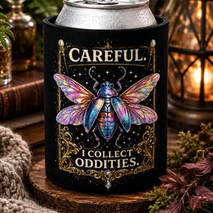 May include: A black foam can cooler featuring a colourful, iridescent beetle illustration with spread wings. The text CAREFUL. I COLLECT ODDITIES. is printed in gold lettering above and below the insect, framed by ornate gold filigree borders.
