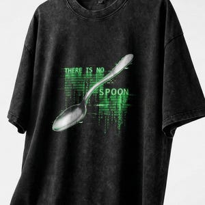 May include: Black t-shirt with a distressed finish. The shirt features a silver spoon graphic and the text "THERE IS NO SPOON" in green, stylized to resemble computer code. The design is centered on the front of the shirt.