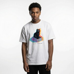 Puede incluir: Camiseta blanca con un gr&aacute;fico de un gato negro dentro de una caja con un efecto 3D colorido. El texto "think outside" est&aacute; debajo. La camiseta tiene mangas cortas y cuello redondo.
