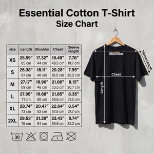 Puede incluir: Camiseta esencial de algod&oacute;n negro colgada de una percha de madera. La imagen incluye una tabla de tallas con medidas en pulgadas y cent&iacute;metros para largo, hombro, pecho y largo de manga. Tambi&eacute;n se incluyen instrucciones de lavado.