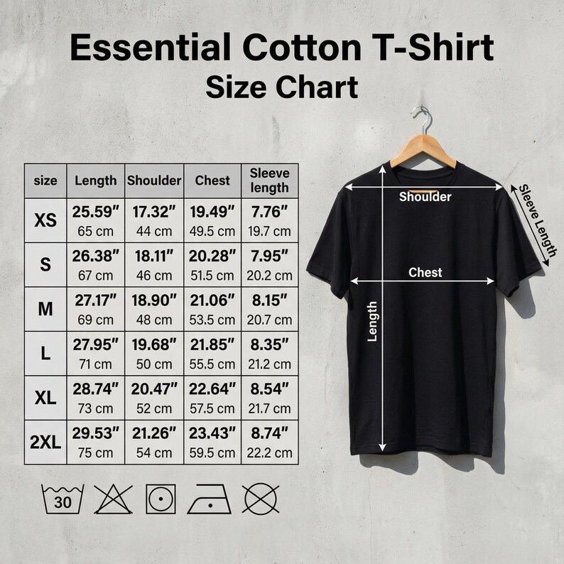 Puede incluir: Camiseta esencial de algod&oacute;n negro colgada de una percha de madera. La imagen incluye una tabla de tallas con medidas en pulgadas y cent&iacute;metros para largo, hombro, pecho y largo de manga. Tambi&eacute;n se incluyen instrucciones de lavado.