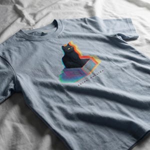 Puede incluir: Camiseta azul claro con un gr&aacute;fico de un gato negro saliendo de una caja con un efecto 3D colorido. El texto "think outside" est&aacute; impreso en blanco debajo. La camiseta est&aacute; hecha de un material suave.