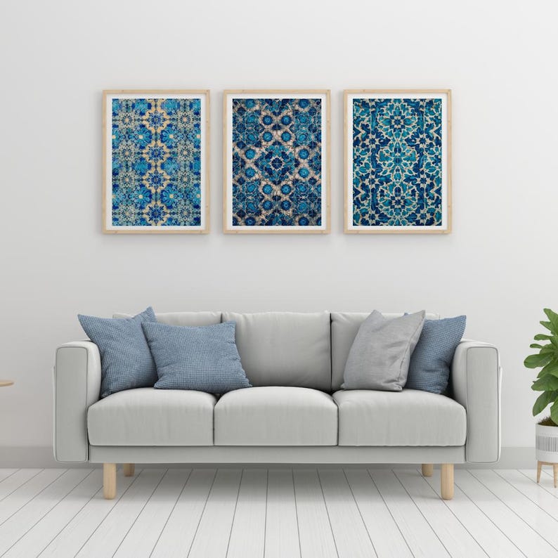 May include: Three framed wall art prints with intricate blue and white patterns. The prints are displayed above a gray sofa with blue and gray pillows. The room has a neutral color palette with a white wall and light wood floors.