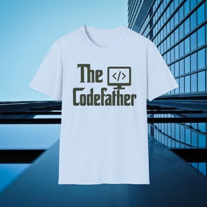 Op de afbeelding: Wit T-shirt met de tekst "The Codefather" in donkergrijs. Het ontwerp bevat een computerbeeldschermpictogram met codesymbolen. Het T-shirt heeft een ronde hals.