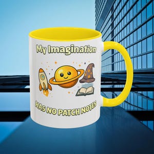 Puede incluir: Taza de cerámica blanca con interior y asa amarillos. La taza presenta el texto "My Imagination Has No Patch Notes" e ilustraciones de un cohete, un planeta, un sombrero de mago y un libro abierto.
