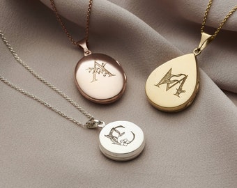 May include: Three gold locket necklaces with different initial engravings and floral designs. The lockets are oval, teardrop, and round in shape. The necklaces are on a light brown fabric background.