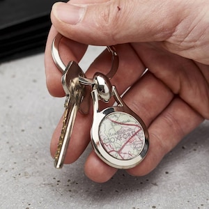May include: Silver-toned keychain with a circular pendant featuring a map of Oxford, England. The keychain holds two keys. The map design includes red roads and the city name. The keychain is held against a gray background.